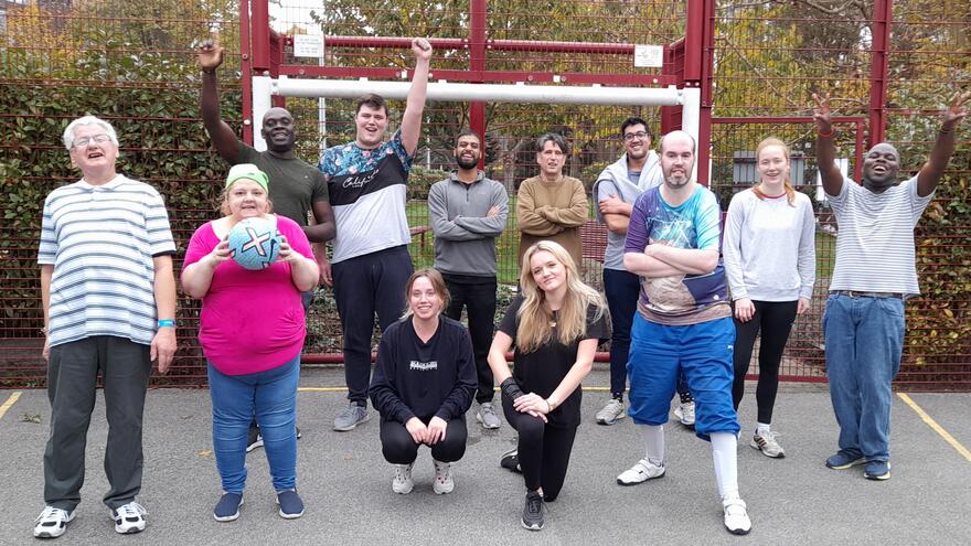 A group of people stand in front of a football goal. They are cheering and smiling.